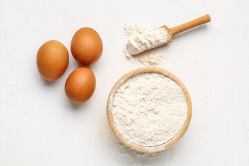 Wooden bowl with wheat flour, scoop and eggs on white background