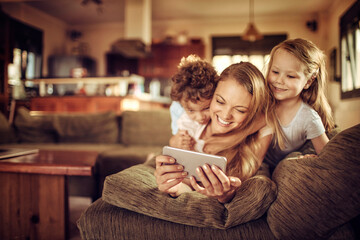 Mother and her two kids using a smart phone to take a selfie on the couch in the living room