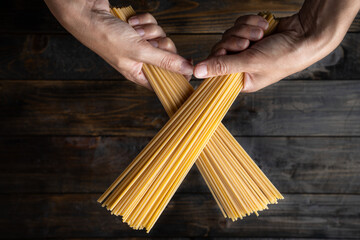 Raw uncooked Italian pasta spaghetti held in two hands over a dark wooden background