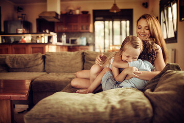 Fototapeta premium Single mother playing with her son and daughter on the couch in the living room