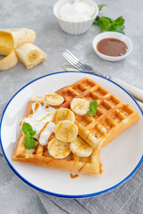 Waffles with banana, whipped cream and salty caramel on a gray concrete background.
