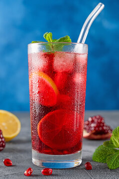 Iced red lemonade drink with fresh mint, sugar syrup and pomegranate juice in glass on a dark concrete background. Refreshing summer drink. Copy space.
