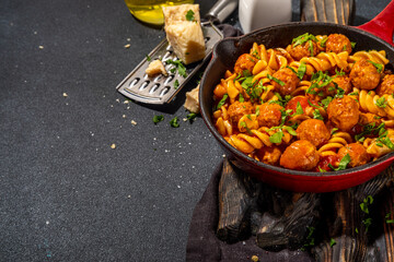 Fusilli pasta with meatballs in tomato vegetable sauce, on dark background with herbs and grated cheese, top view copy space