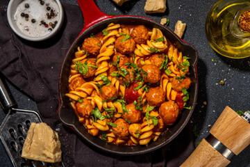 Fusilli pasta with meatballs in tomato vegetable sauce, on dark background with herbs and grated cheese, top view copy space