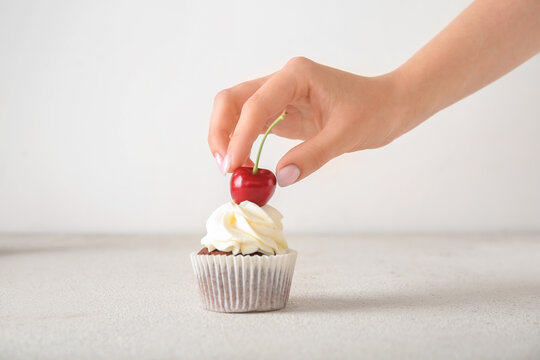 Woman decorating tasty cupcake with cherry on light background