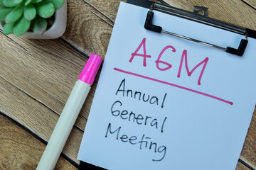 Concept of AGM - Annual General Meeting write on paperwork isolated on Wooden Table.