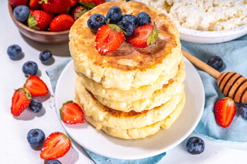Sweet homemade cottage cheese pancakes, american version of syrniki or cottage cheese fritters, big pan fried cheesy pancakes with fresh summer blueberry and strawberry, healthy high-protein breakfast