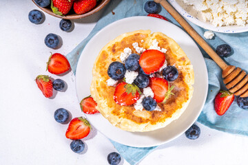 Sweet homemade cottage cheese pancakes, american version of syrniki or cottage cheese fritters, big pan fried cheesy pancakes with fresh summer blueberry and strawberry, healthy high-protein breakfast