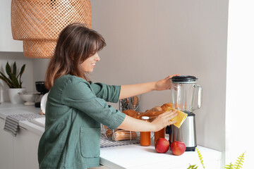 Young woman cleaning modern blender in light kitchen