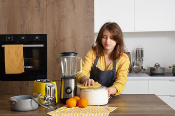 Young woman in kitchen cleaning juicer on wooden table