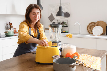 Young woman in kitchen cleaning toaster on wooden table