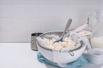 Making cottage cheese, homemade fermenting dairy product. Homemade cottage cheese in cheesecloth bags on kitchen table, woman hands drain cheese at home top view copy space