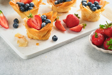 Phyllo or filo pies with fresh berries strawberries and blueberries, cheese filling topped with fresh mint on white plate. Homemade Filo pastry paskets. Delicious filo pastry dessert.