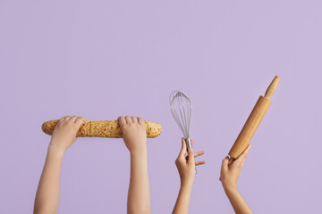 Female hands with baguette, whisk and rolling pin on lilac background