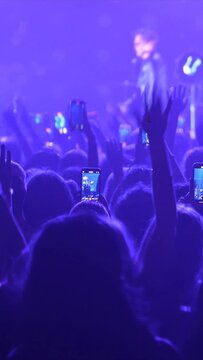 Vertical video slow motion of unrecognizable fans dancing at a concert or festival party. Silhouettes of concert crowd in front of bright flashing strobe stage lights