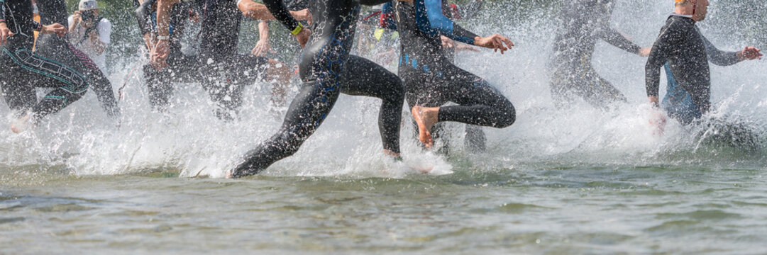 Triathletes in wetsuits running into a lake at a triathlon competition