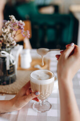 A drop of milk foam that is lifted by a spoon from a glass of Latte coffee, on which there is a brown cloth napkin with a wooden stand for salt, pepper, sugar and napkins near