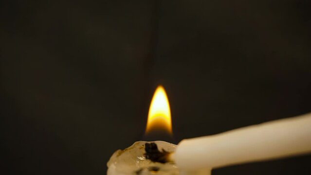 Encender una vela blanca gruesa con una vela blanca delgada en fondo oscuro horizontal 
