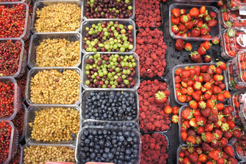 Ripe berries in containers in the market. Strawberries, raspberries, currants, blueberries, gooseberries in the store counter. Top view.