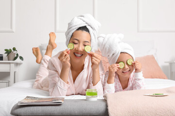Asian mother with her little daughter and cucumber slices in bedroom