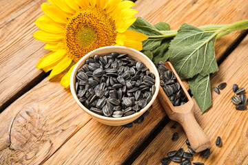 Beautiful sunflower and bowl with seeds on wooden background