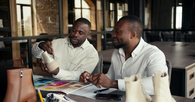 Two Black-skinned businessmen in white shirts are discussing the sole for a new shoe in the office of a shoe factory