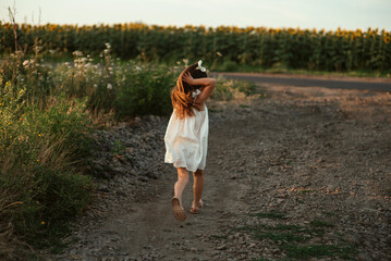 Cute little girl in white summer dress running towards a field of sunflowers. Back view