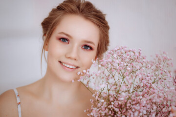 Face of a beautiful young smiling woman close up. Pale pink flowers on the face. The concept of natural skin care cosmetics or women's holiday.