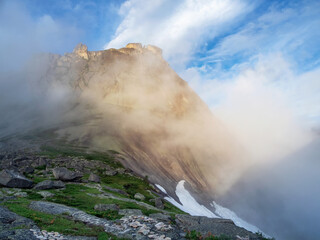 Soft focus. Sunrise in the mountains, in thick clouds. Light on the pass. The glacier is melting, illuminated by the bright golden morning sun.