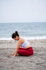 Fototapeta na wymiar Concentrated beautiful woman in sportswear stretching on the beach