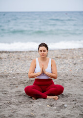 Fototapeta na wymiar Beautiful woman in lotus pose doing yoga at the beach with palms together and closed eyes
