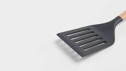 Closeup view of heat-resistant plastic spatula with wooden grip on light grey copy-space background.