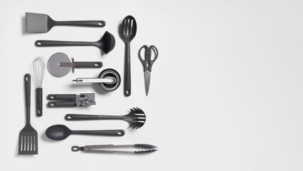 Top view closeup of twelve laid out pieces of soft handle kitchen utensils on copy-space light grey background.