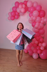 criança sorridente com muitas sacolas de compras, expressão positiva e alegre , fundo festivo com...