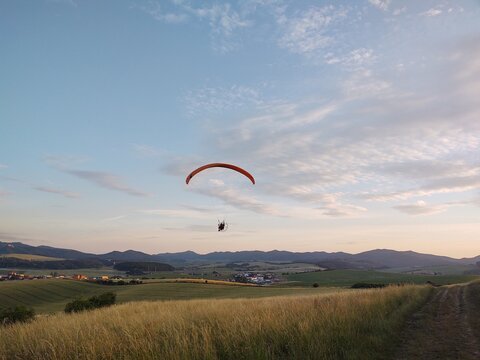 Paraglider flying on the parachute during sunset on the meadow.