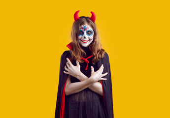 Portrait of teen girl with creative Halloween skull makeup. Beautiful teenager wearing red horns...