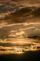 Fototapeta premium large orange clouds in the blue sky, during the golden hour, through which the bright rays of the sun break through