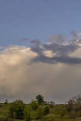 green tree tops, against the backdrop of a huge large white cloud and a small gray cloud in front of it
