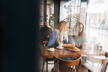 Obraz premium View from door glass to upset young woman telling best friend about boyfriend betrayal. Compassion showed to real best girlfriends. Life problem concept. Gossiping along with friend at coffee shop.