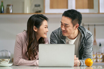 young asian couple using laptop computer together at home
