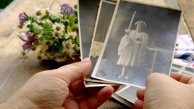 female hands holding paper envelope with old photographs, bouquet of wild flowers on table wooden table in garden, blurred natural background, concept of genealogy, memory of ancestors, family tree