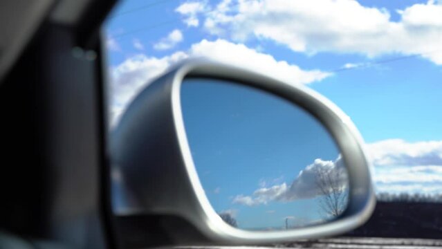 Clouds are reflected in the rear mirror of the car