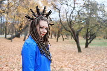 A middle-aged woman in dreadlocks and a hoop on her hair in feathers walks in the autumn park....