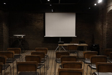 empty Conference room with many chairs and projection screen. modern classroom with white walls, wooden floor, rows of chairs and mock up projection screen and whiteboard.