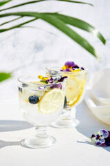 Cold water with lemon garnished with edible flowers. Cool summer lemonade. Summer non-alcoholic cocktails and drinks.