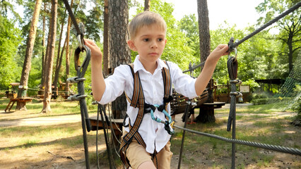 Portrait of little boy crossing the rope bridge between two trees in park