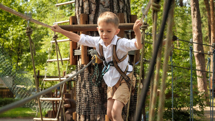 Happy smiling boy having fun climbing and crossing obstacles in rope park. Active childhood,...