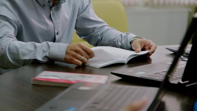 Close-up image of a university professor's desk preparing to start the lesson. Male professor at the prestigious law school browsing a code and explaining something to the students.