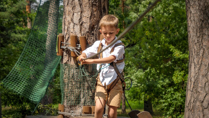 Portrait of concentrated boy holding safety rope while crossing bridge in outdoor summer camp. Active childhood, healthy lifestyle, kids playing outdoors, children in nature.