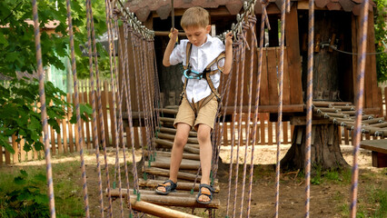 Little boy having fun at extreme adventure park in summer camp. Kids sports, summer holiday, fun outdoors, scouts.